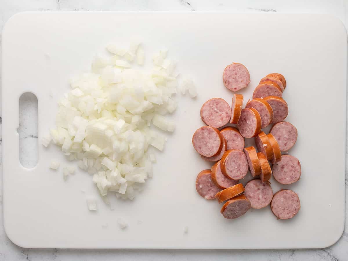 Diced onion and sliced sausage on a cutting board. 
