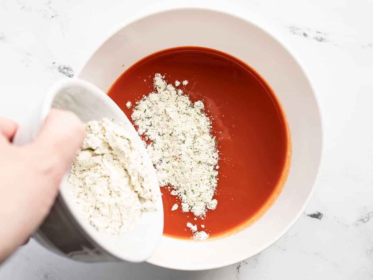 ranch seasoning being poured into a bowl of hot sauce