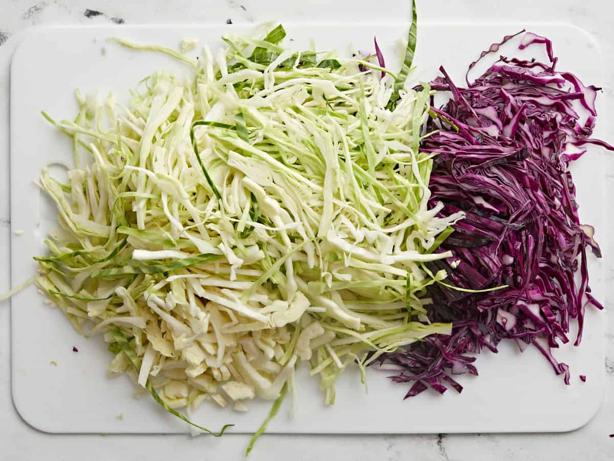 Shredded green and purple cabbage on a cutting board. 