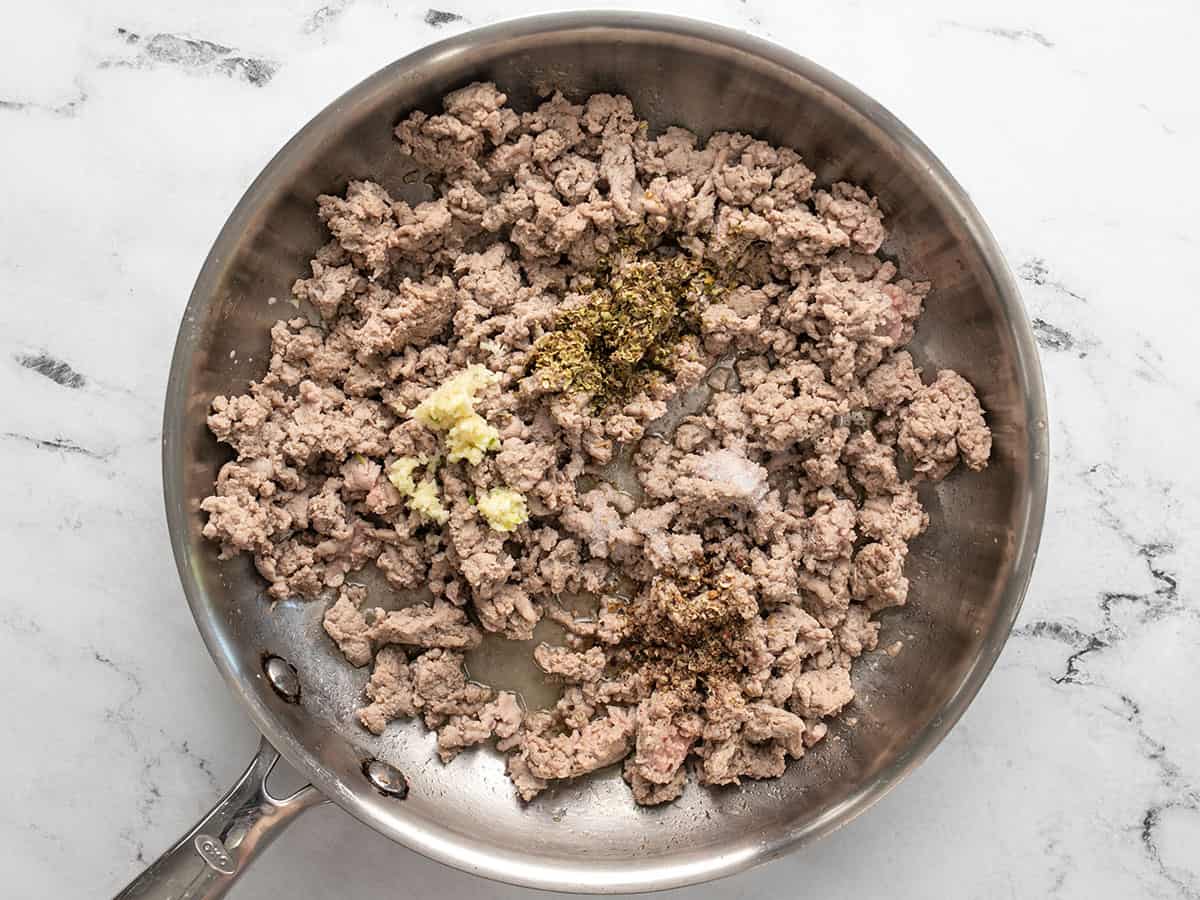 Cooked ground turkey in a skillet with garlic and oregano added on top.