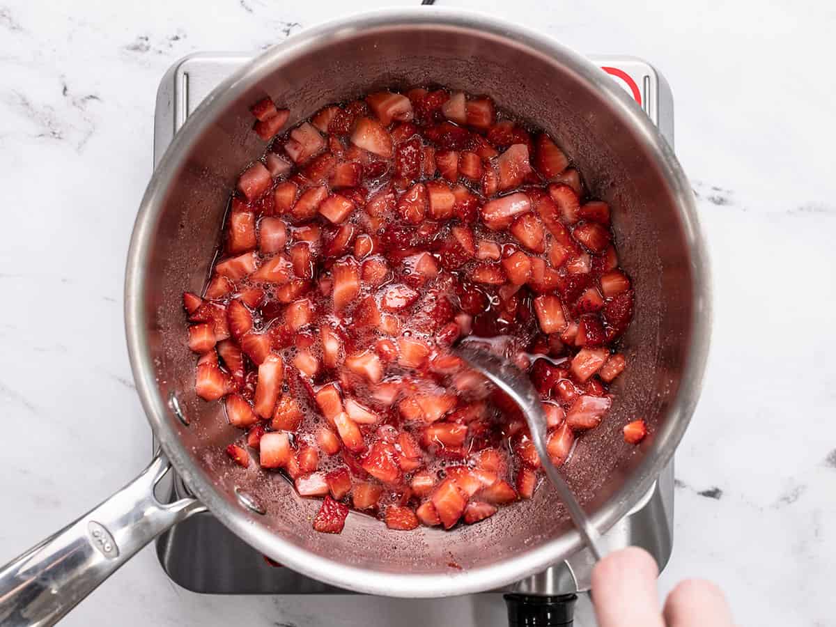 Strawberries and sugar being stirred in the pot.