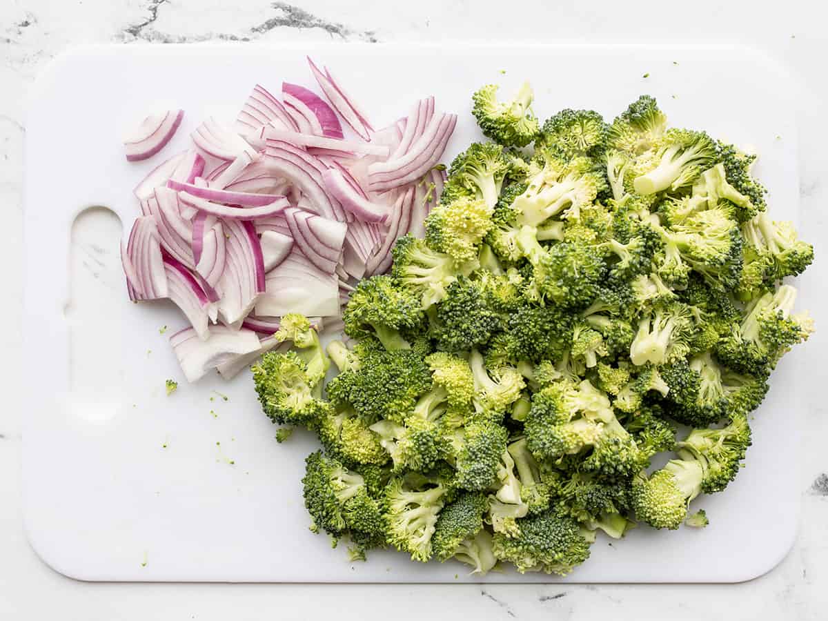 Chopped broccoli and red onion on a cutting board