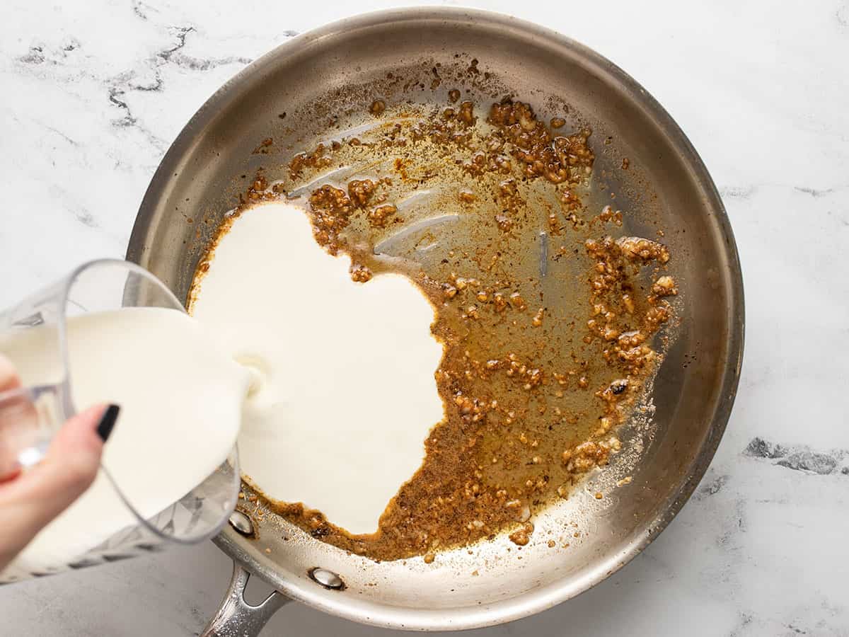 Heavy cream being poured into the skillet.