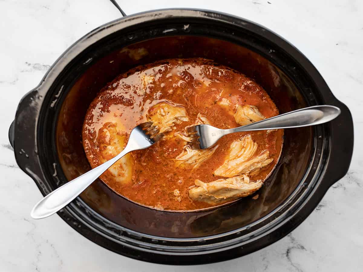 two forks shredding the chicken in the slow cooker
