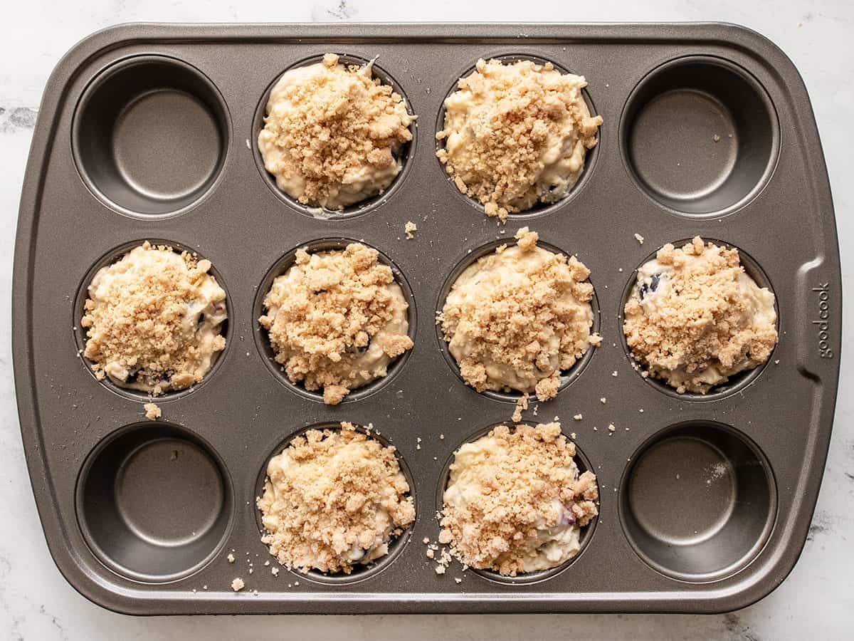 Unbaked blueberry muffins in the muffin tin topped with crumble.