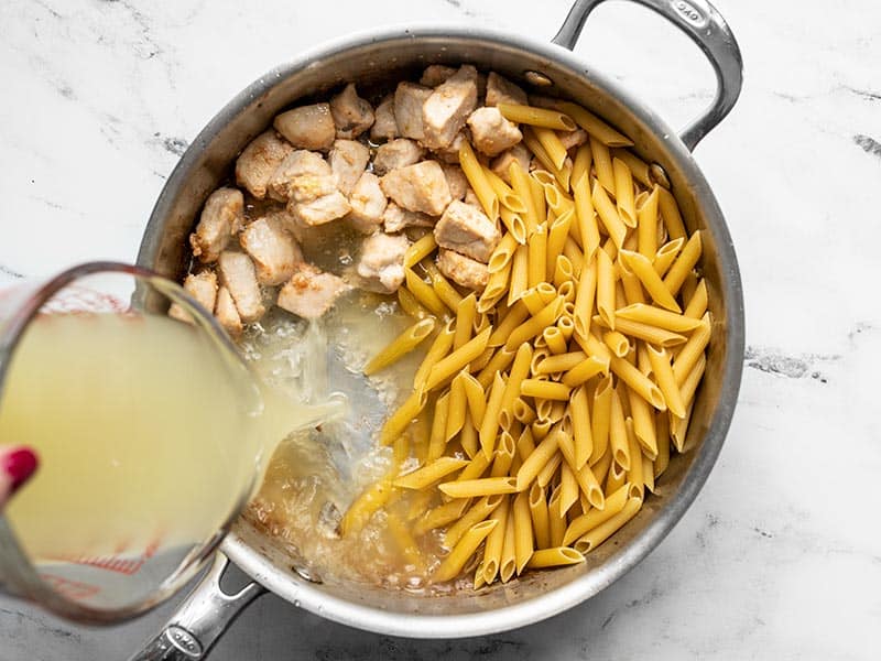 Uncooked pasta and chicken broth added to the skillet