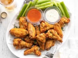 A platter full of baked chicken wings, celery, and two dipping sauces