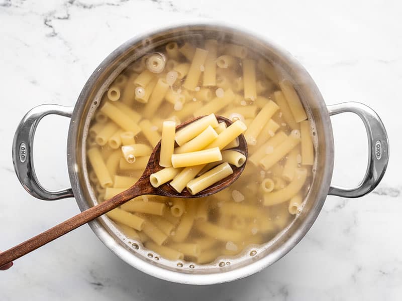 Boiled ziti in a pot of water with a wooden spoon