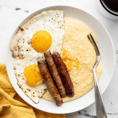 cheese grits in a bowl topped with fried eggs and breakfast sausage