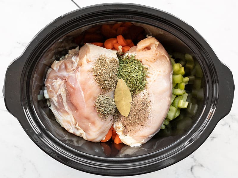 Chicken and herbs added to the slow cooker