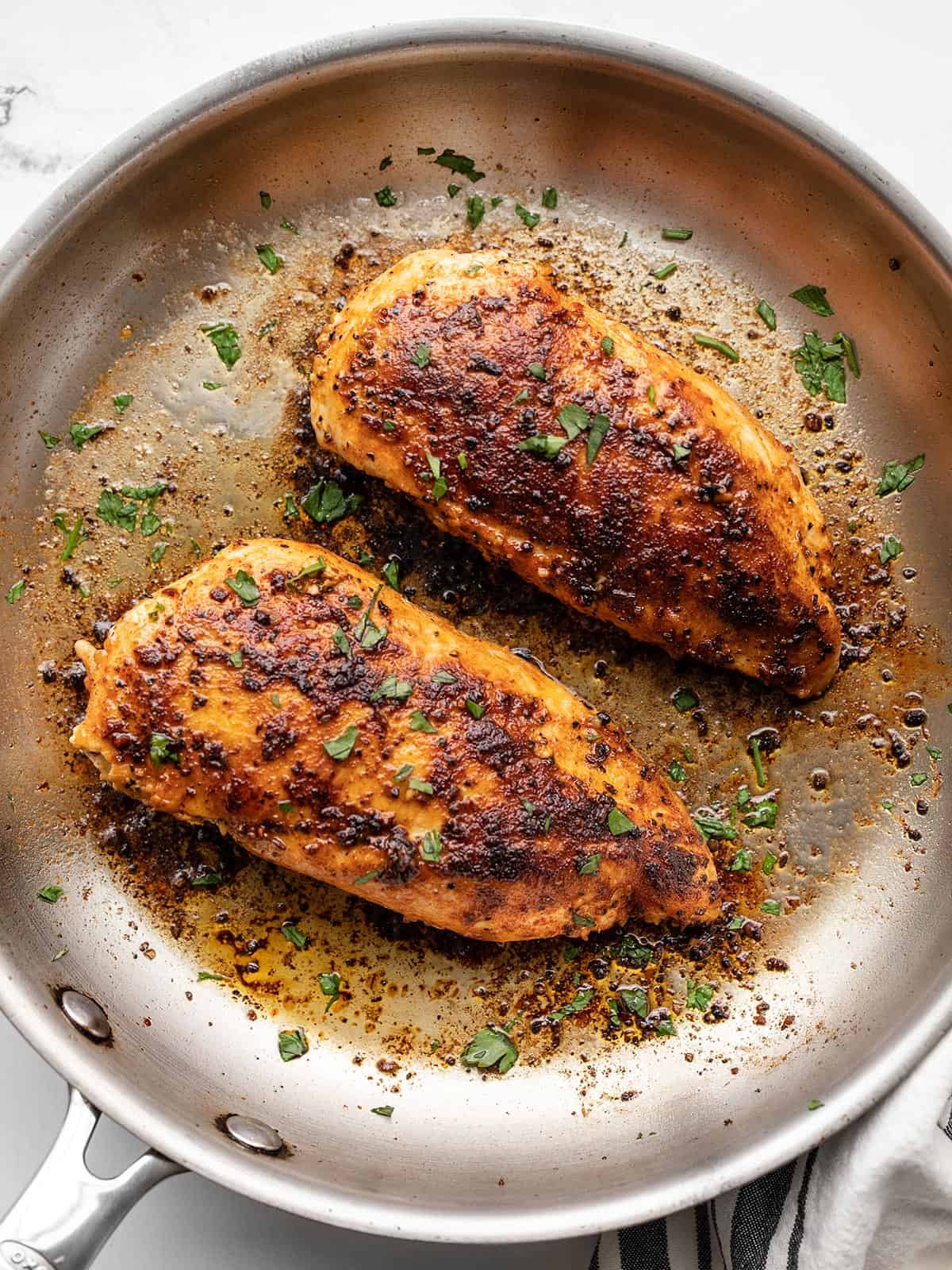 Two chicken breasts in a skillet garnished with parsley