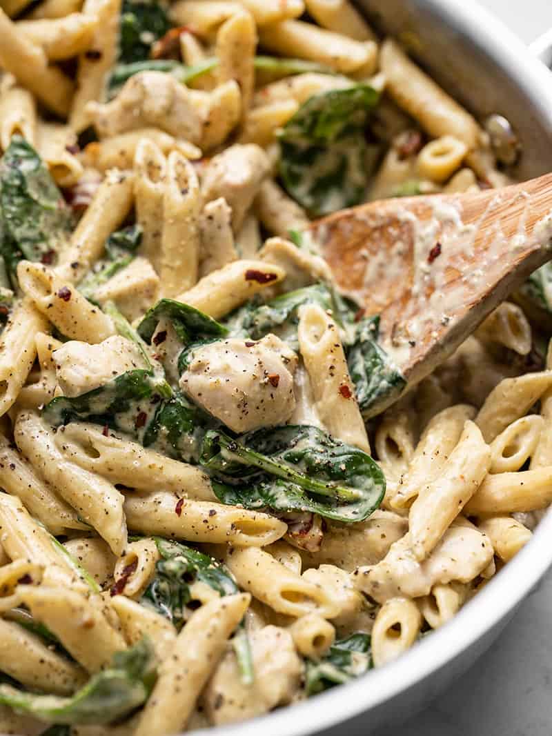 Close up of One Pot Creamy Pesto Chicken Pasta in the skillet with a wooden spoon