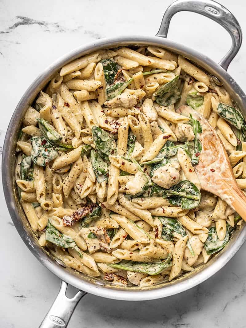 Overhead view of a skillet full of one pot creamy pesto chicken pasta with a wooden spoon in the side.