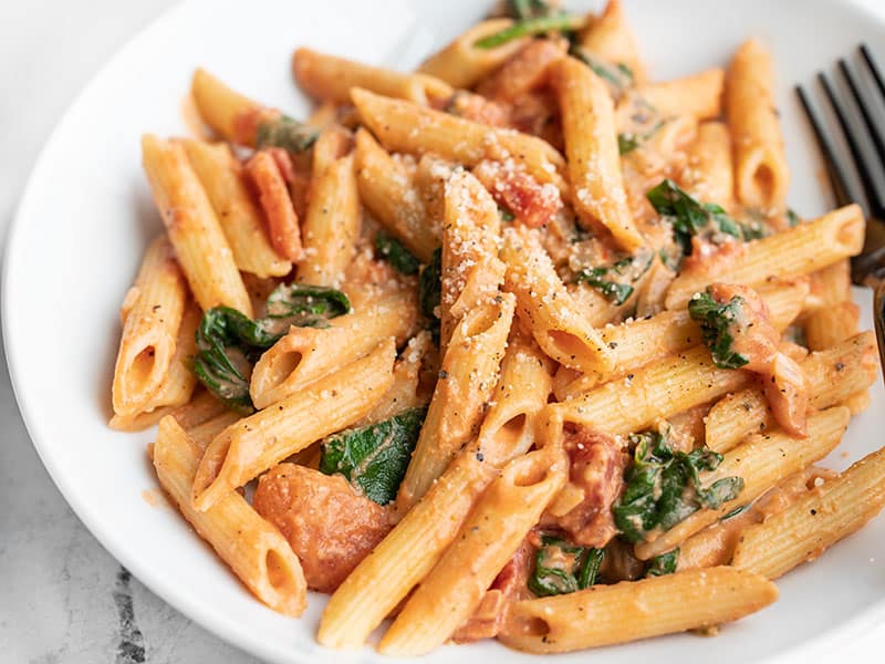 Close up side view of a bowl of creamy tomato and spinach pasta