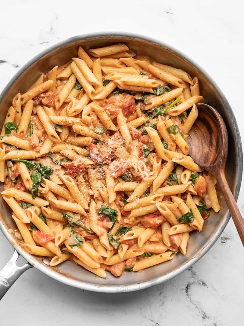 Overhead view of the creamy tomato and spinach pasta in the skillet with a wooden spoon.