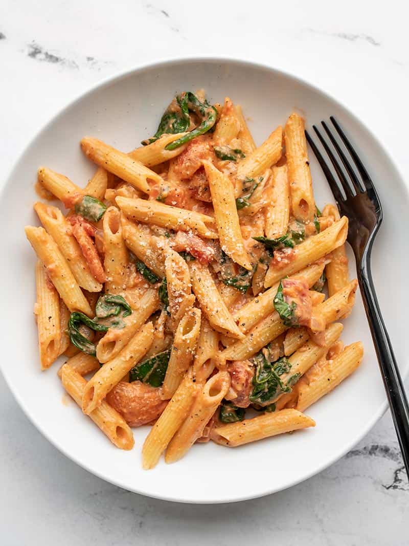 Overhead view of a bowl of creamy tomato and spinach pasta, with a black fork in the side