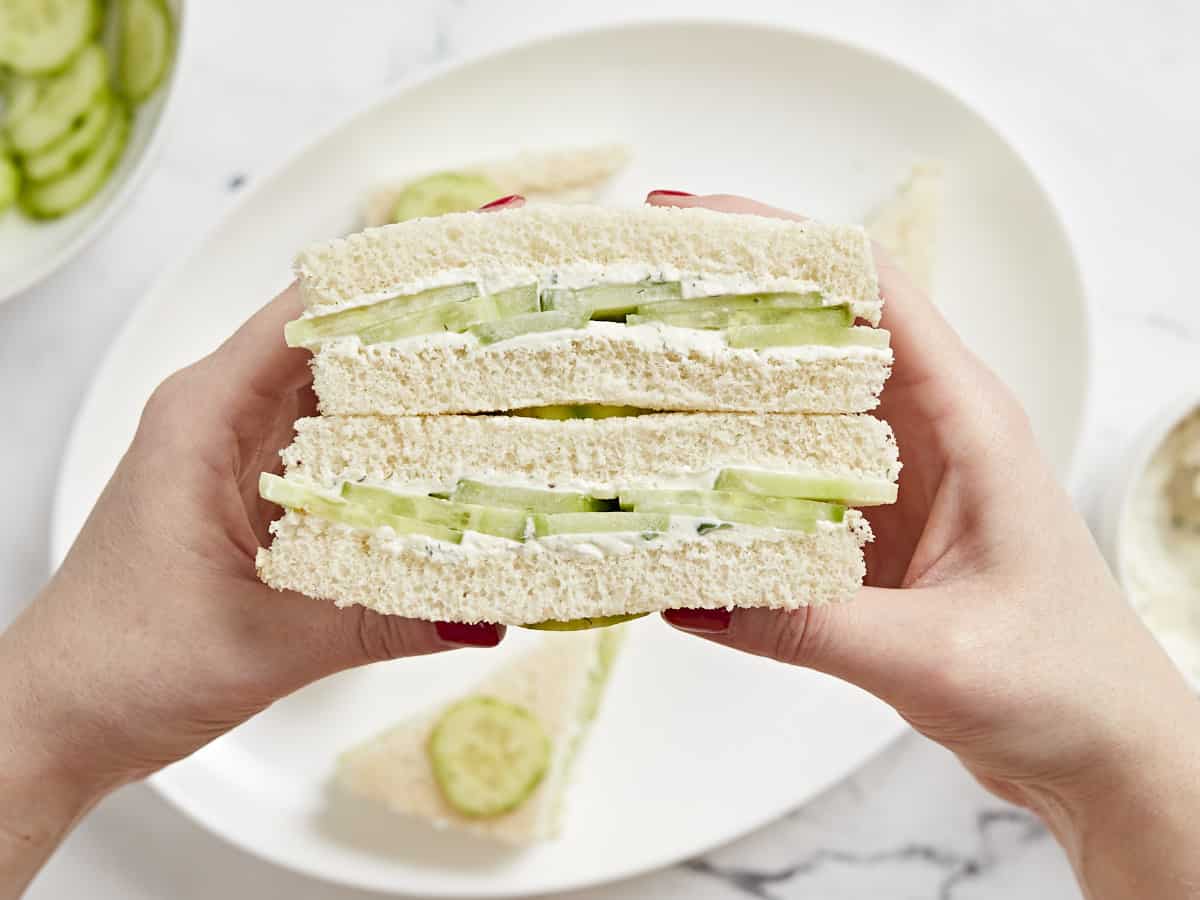 Side view of hands holding a stacked cucumber sandwich.
