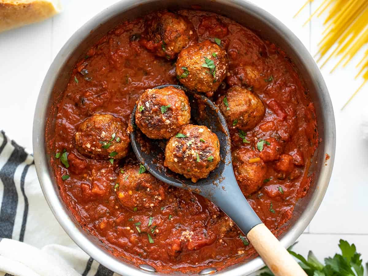 Meatballs in a pot of red sauce with a spoon holding two meatballs