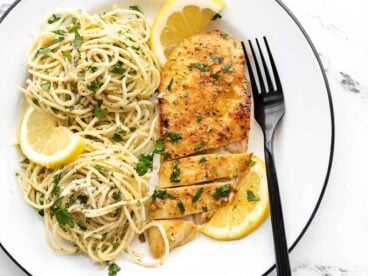 A sliced piece of lemon pepper chicken on a plate with pasta.