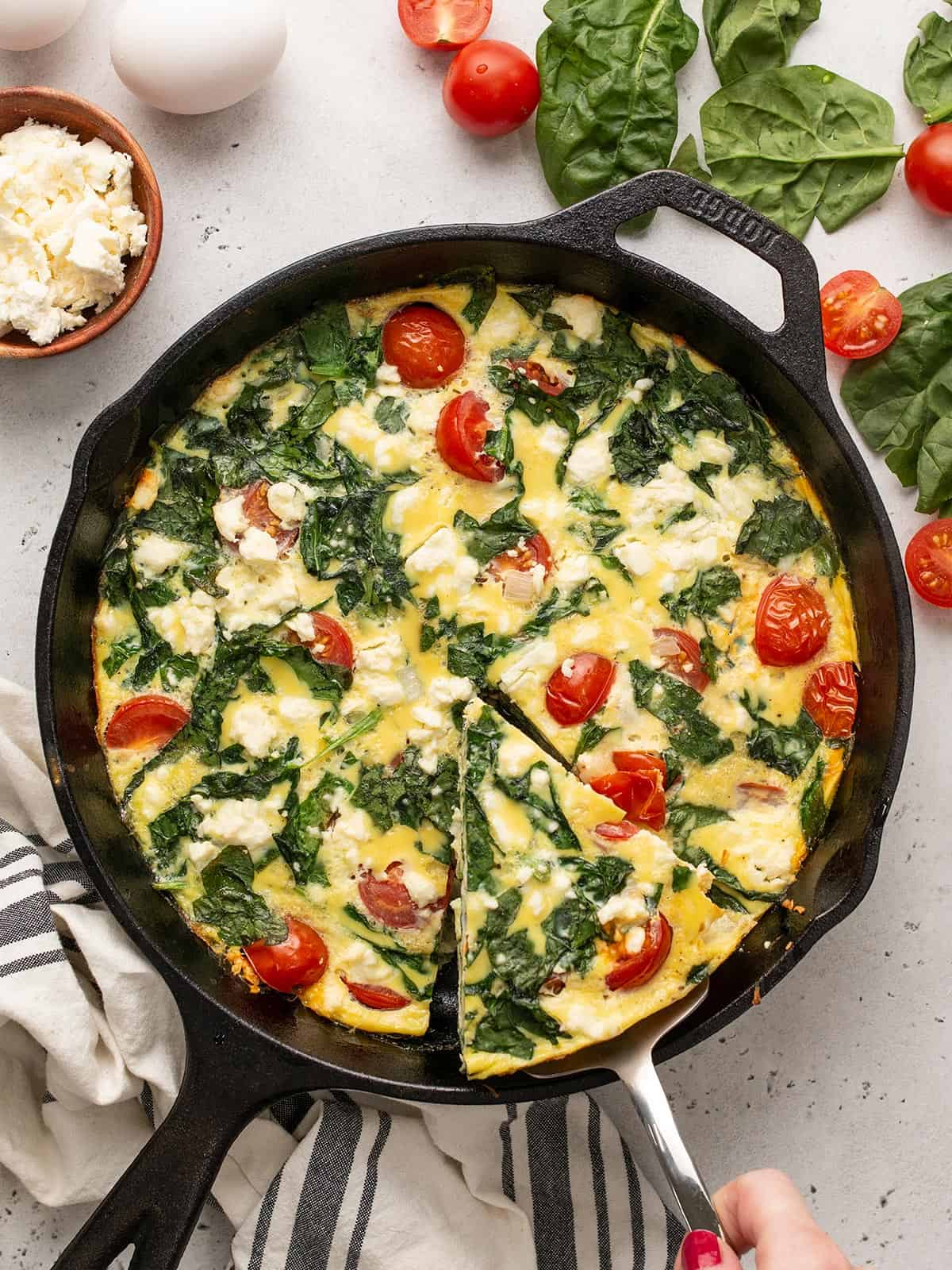 A slice of frittata being lifted out of a cast iron skillet.