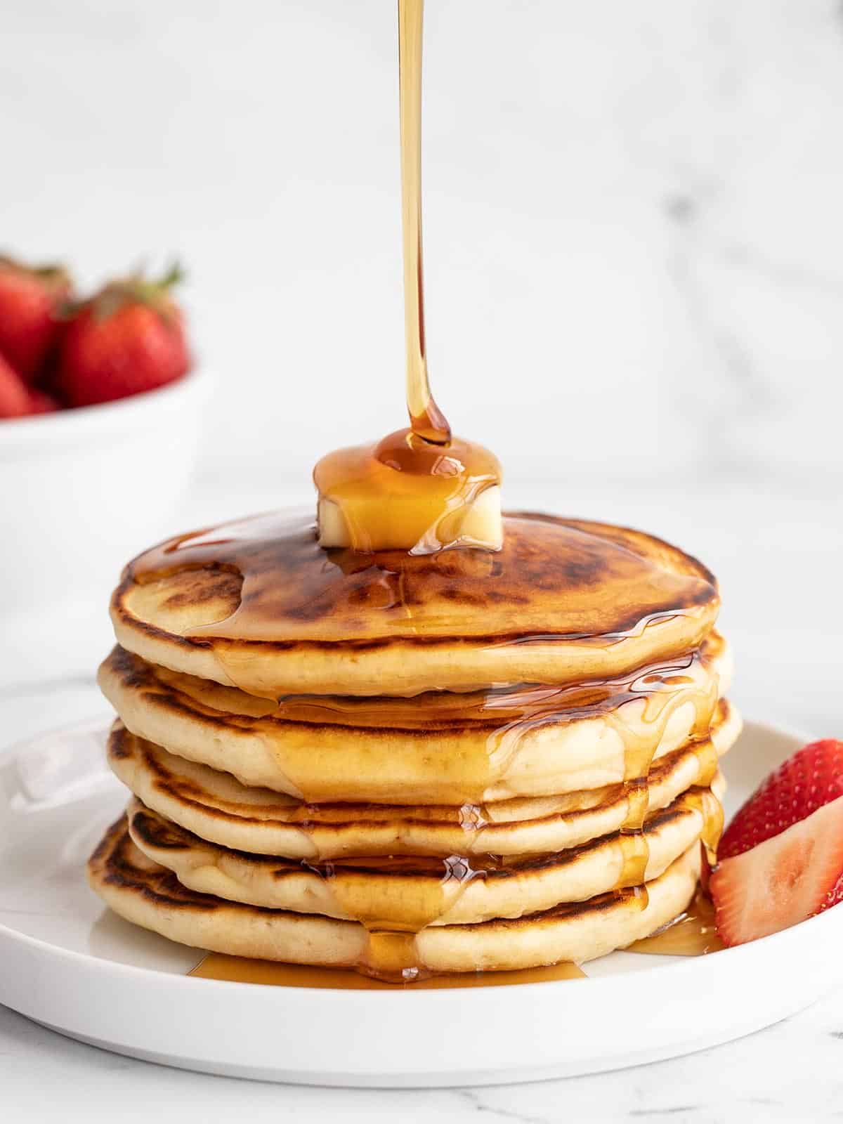 Syrup being poured onto a stack of pancakes.