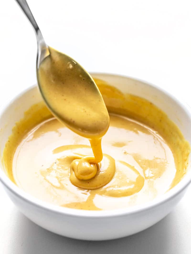 Honey Mustard Sauce dripping off a spoon into a white bowl.