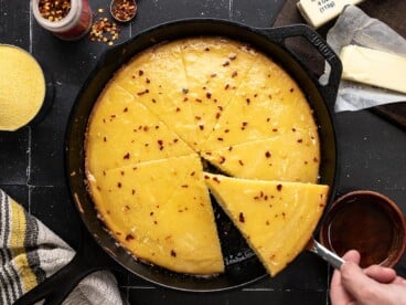 Overhead shot of hot honey cornbread in a cast iron skillet with a wedge being taken out.
