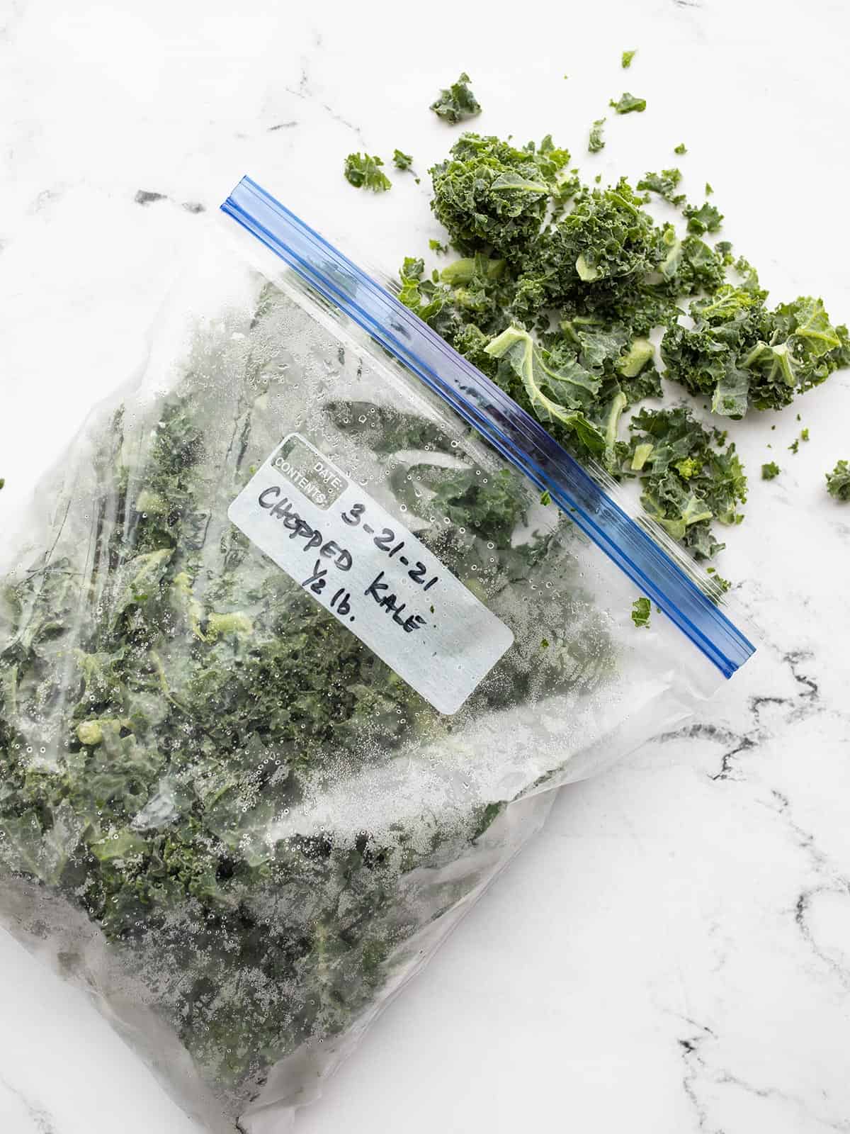 A freezer bag of kale spilling out onto a marble surface