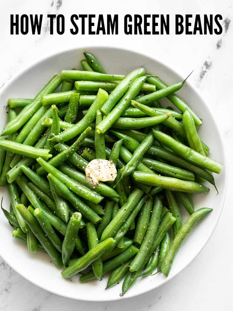 Overhead view of a bowl full of steamed green beans with butter, salt, and pepper