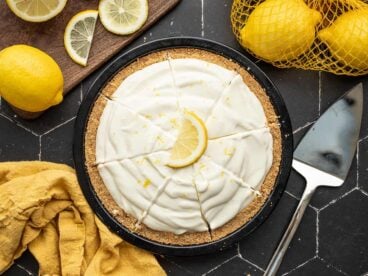 Overhead view of a sliced lemon cream pie with lemons on the sides