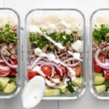 Three meal prep turkey bowls lined up with yogurt sauce being drizzled over the middle one.