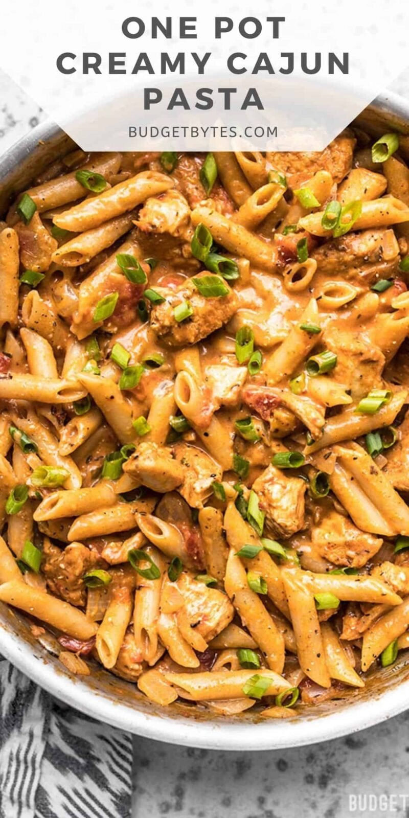 Overhead view of cajun chicken pasta in the skillet, title text at the top