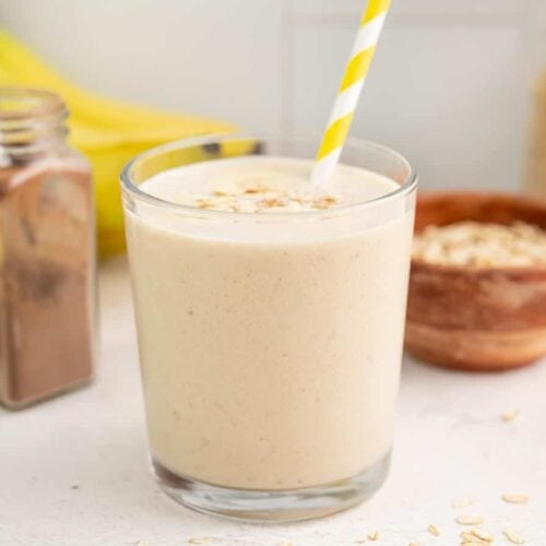 Side view of a glass full of peanut butter banana smoothie with a yellow striped straw.