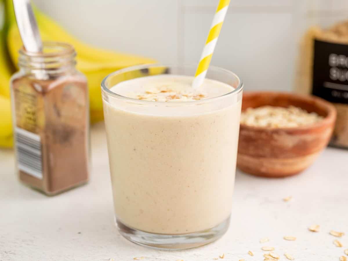 Side view of a glass full of peanut butter banana smoothie with a yellow striped straw.