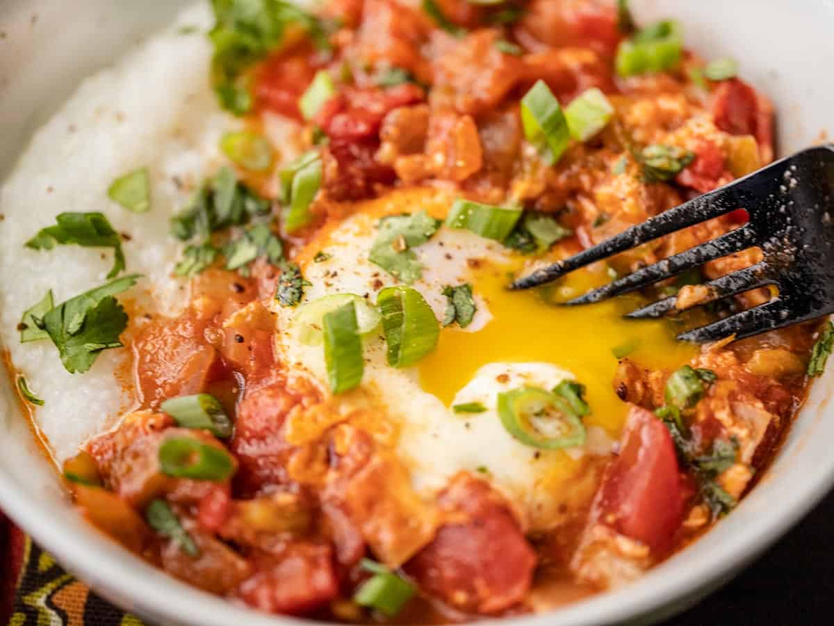 close up of the yolk being broken with a fork in a bowl of salsa and grits