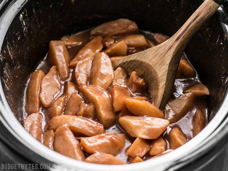 Slow Cooker Hot Buttered Apples in the slow cooker with a wooden spoon