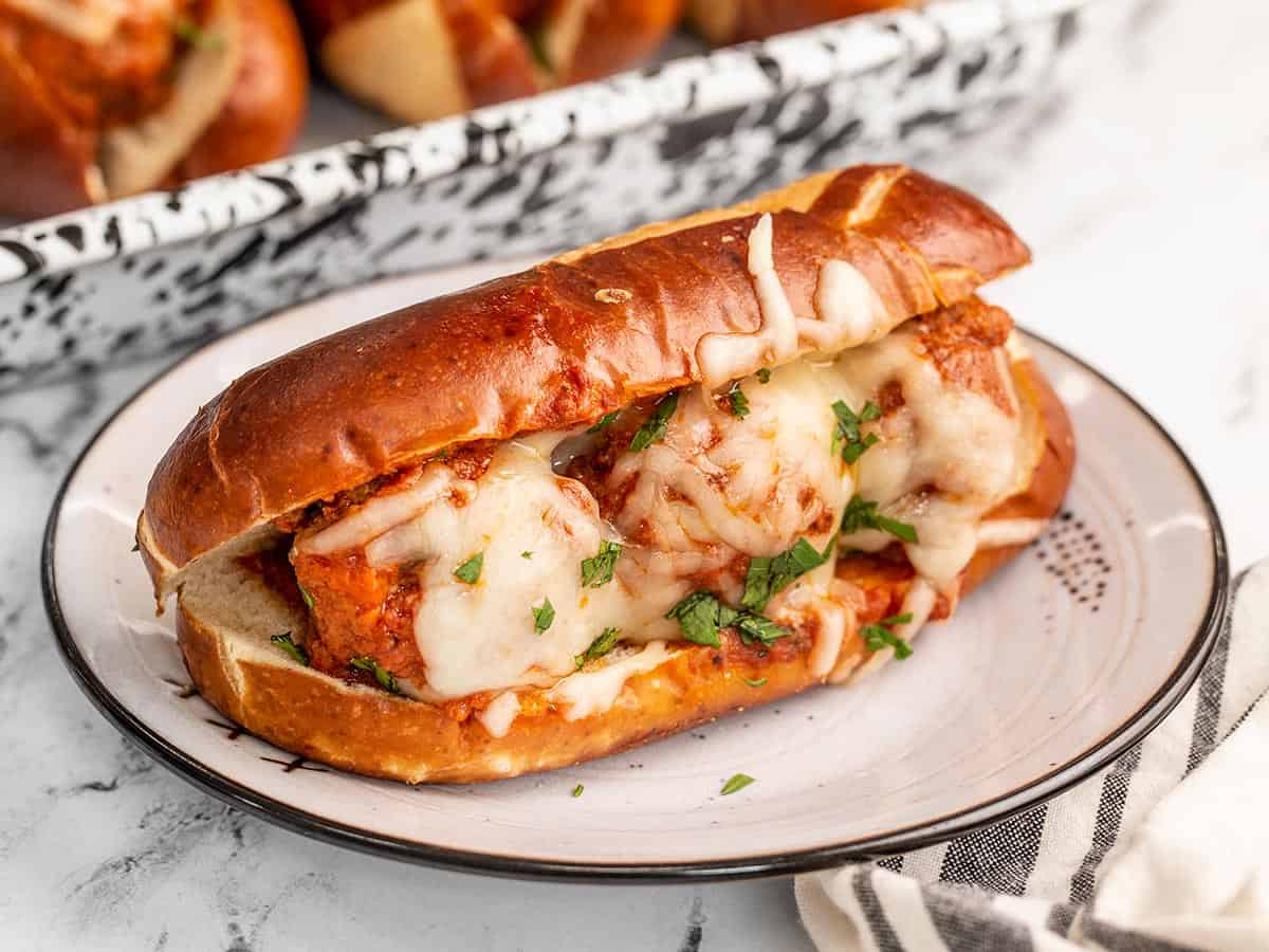 Side view of a meatball sub on a plate with the baking dish in the background.