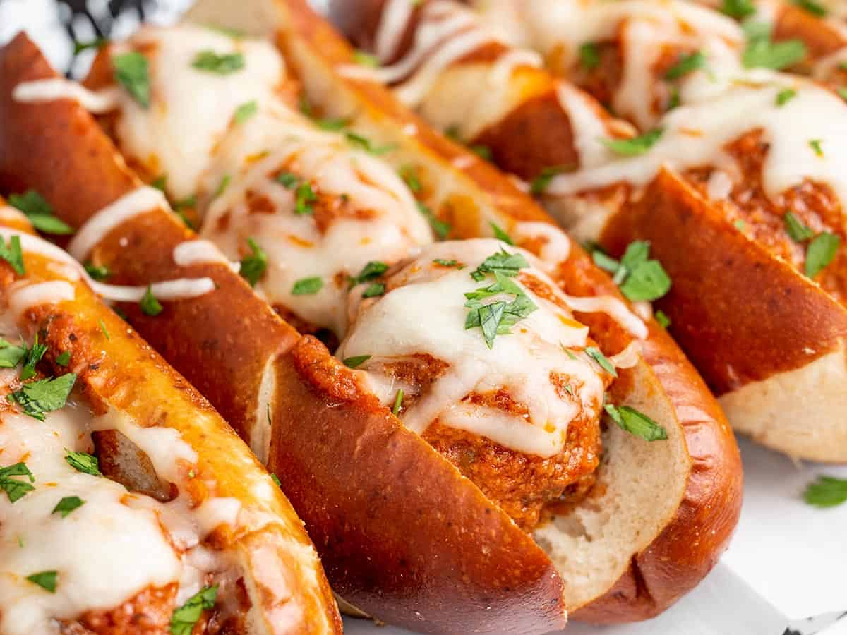 Close up side view of slow cooker meatball subs lined up and garnished with parsley.