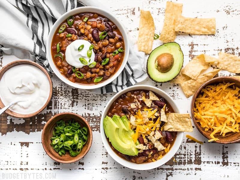 Dressed bowls of Slow Cooker Vegetarian Lentil Chili with various toppings on the side