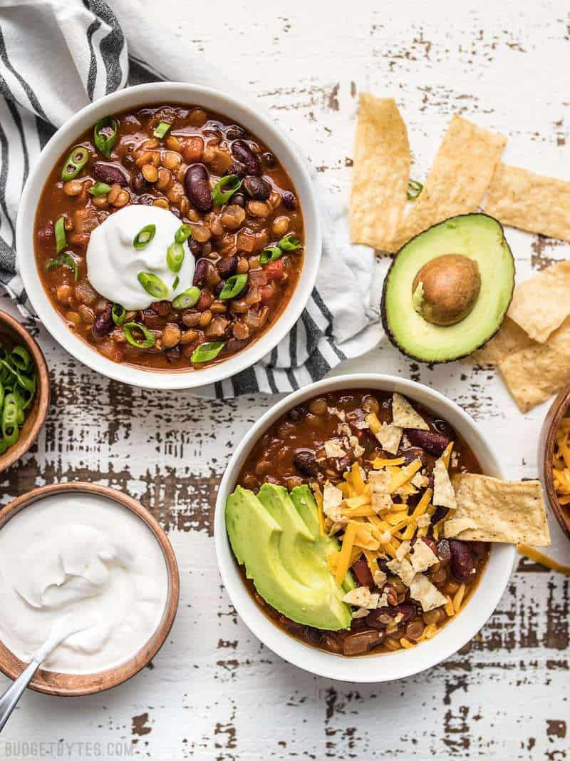 Two bowls of slow cooker vegetarian chili with chips and other toppings