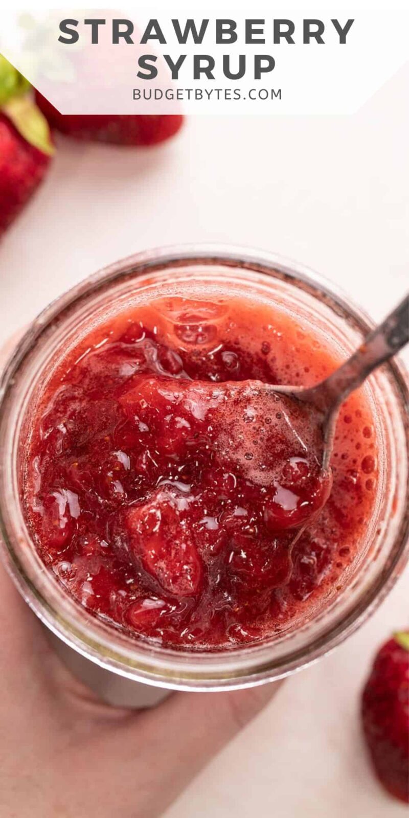 Overhead view of strawberry syrup in a jar with a spoon.