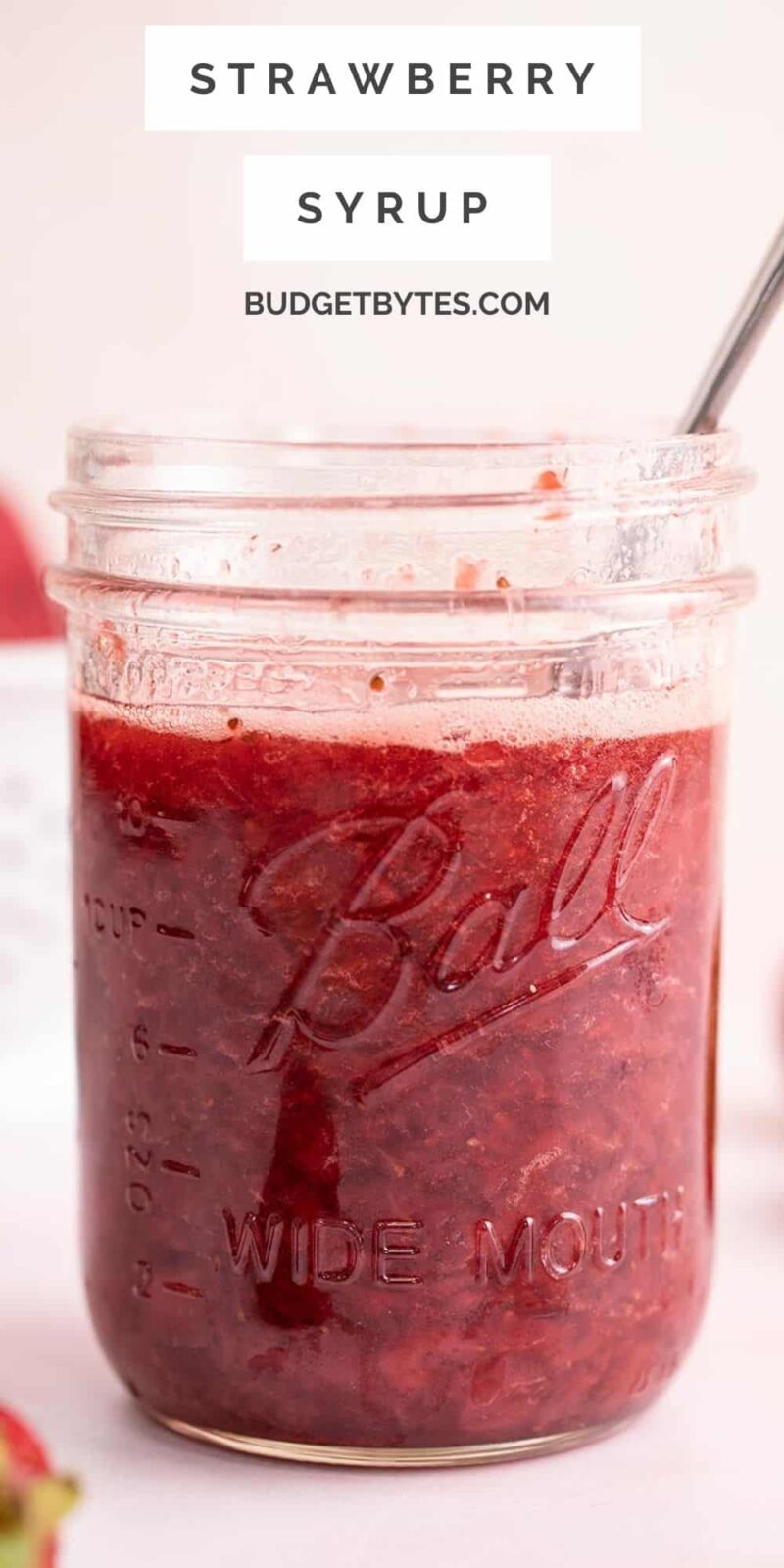 Side view of a jar of strawberry syrup with a spoon.