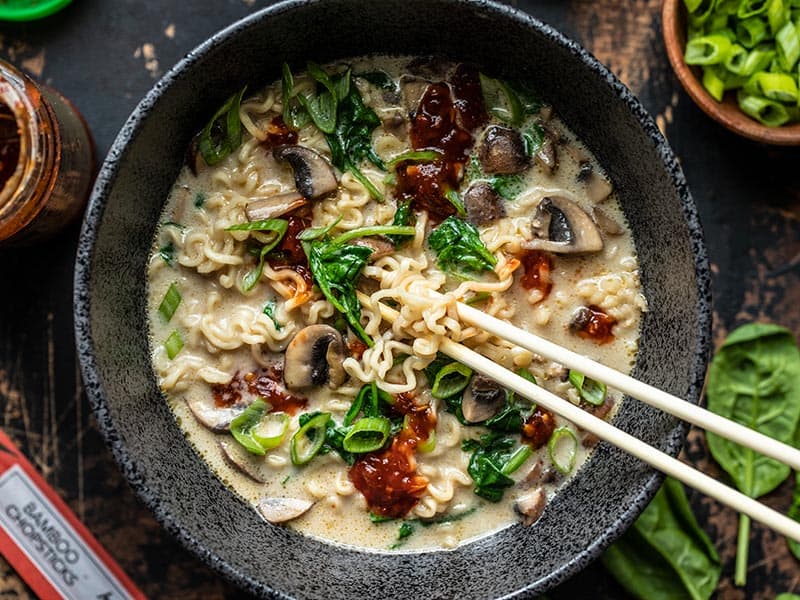 Close up overhead view of a bowl full of vegan creamy mushroom ramen with chopsticks lifting some noodles