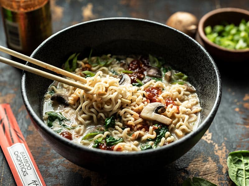 Front view of noodles being lifted out of a bowl of vegan creamy mushroom ramen with chopsticks