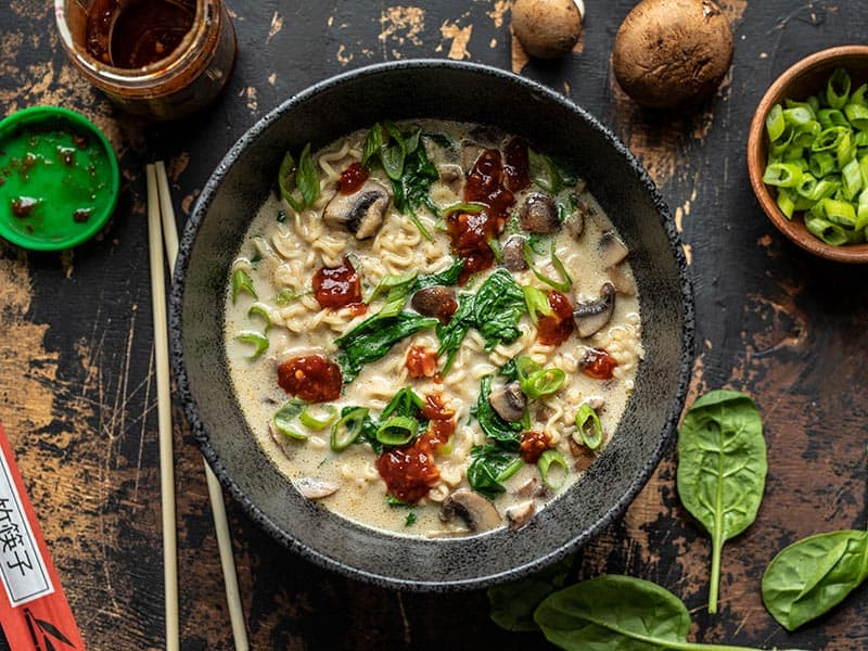 Overhead view of a bowl full of Vegan Creamy Mushroom Ramen garnished with chili garlic sauce and green onion