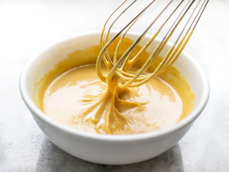 Whisked honey mustard sauce in a bowl with the whisk lifting out of the sauce.